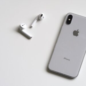 Close-up of a silver iPhone and wireless AirPods on a sleek white background.
